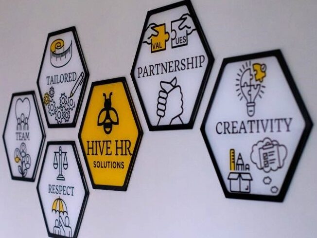 Infographic artwork of an HR company's values displayed in hexagonal tiles on a wall.